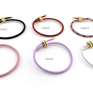 以下が含まれることがあります： 黒、赤、赤と白、ピンク、紫と青、銀色の6色のブレスレット。各ブレスレットには金色の留め金が付いています。ブレスレットは白い表面に表示されています。
