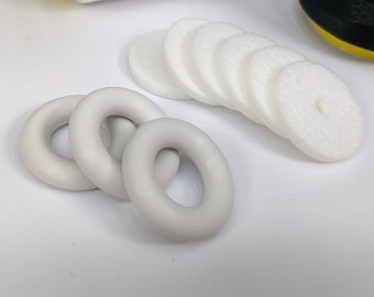 Può includere: Un set di quattro anelli di plastica bianca e un set di otto dischi rotondi bianchi. Gli anelli sono impilati uno sopra l'altro e i dischi sono disposti a semicerchio.