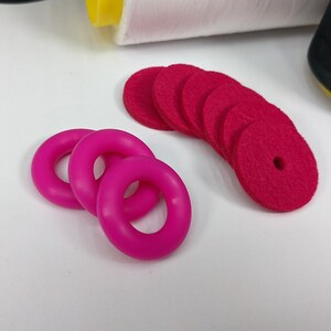 以下が含まれることがあります： ピンクのゴム製のリング4個と、中央に穴が開いた赤いフェルトの円7個のセットです。