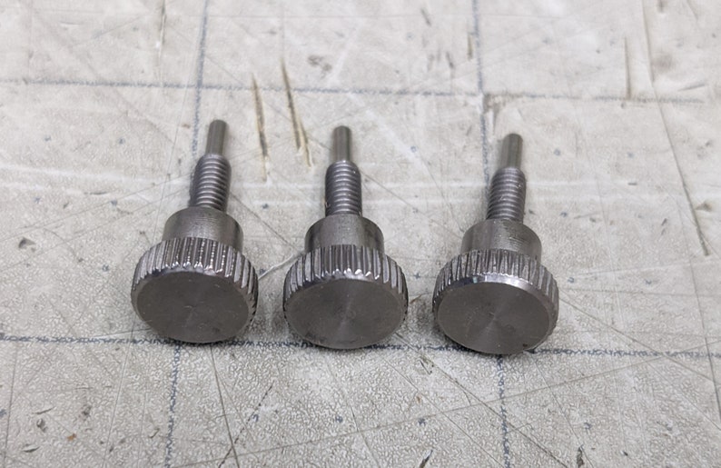 May include: Three silver thumbscrews with a knurled head and a threaded shaft.