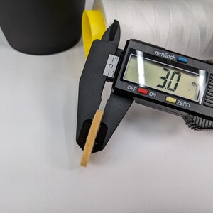 Op de afbeelding: Een zwarte digitale schuifmaat meet een klein, lichtbruin, rond object. De schuifmaat geeft 30 mm aan.