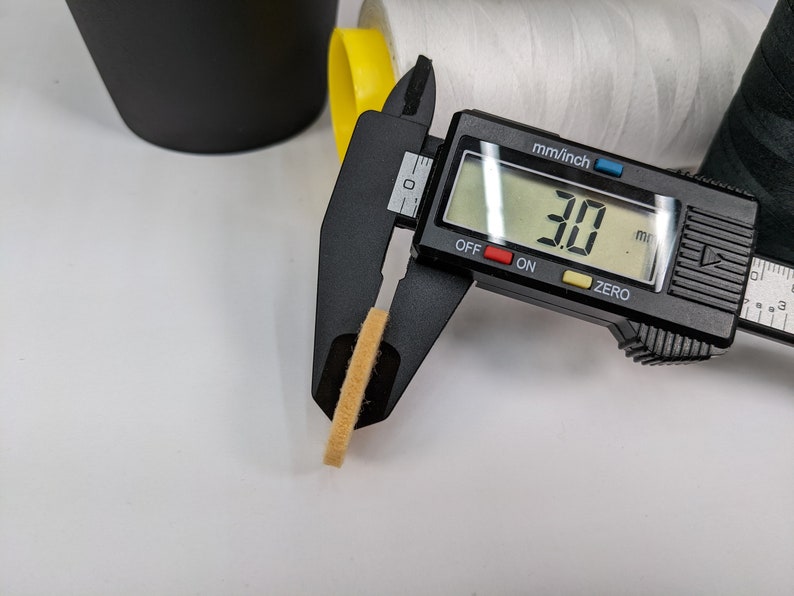 Op de afbeelding: Een zwarte digitale schuifmaat meet een klein, lichtbruin, rond object. De schuifmaat geeft 30 mm aan.