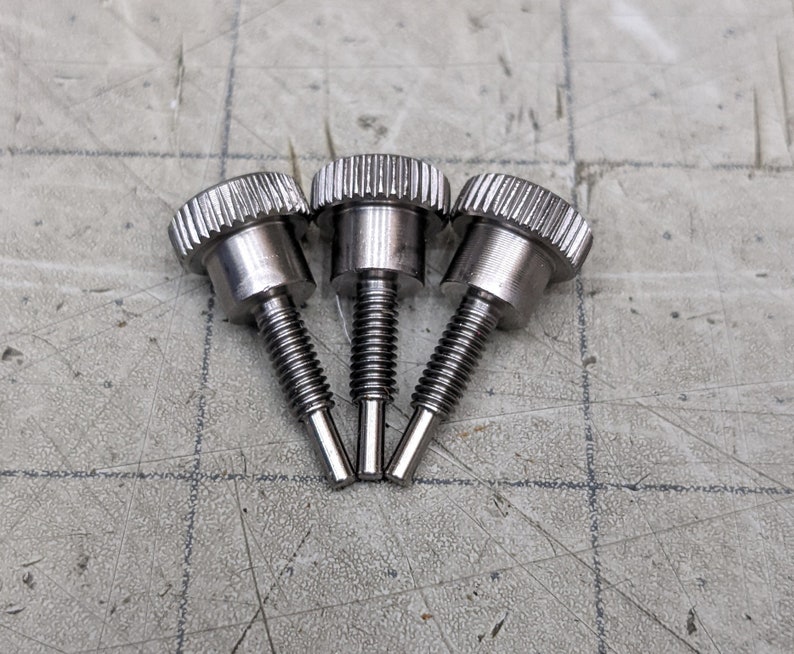 May include: Three silver thumbscrews with knurled heads and a threaded shaft.
