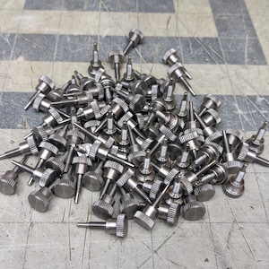 May include: A large pile of silver-colored metal screws with knurled heads. The screws are arranged in a random pattern and are all the same size.