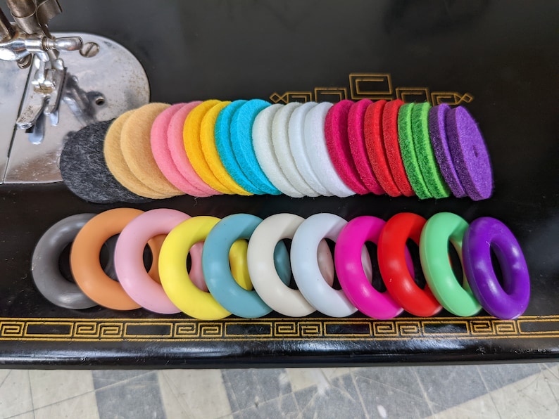 Op de afbeelding: Een set kleurrijke viltcirkel en ringen. De cirkels zijn gestapeld in een regenboogpatroon, terwijl de ringen in een rij zijn gerangschikt. De ringen zijn gemaakt van verschillende materialen, waaronder hout en plastic.
