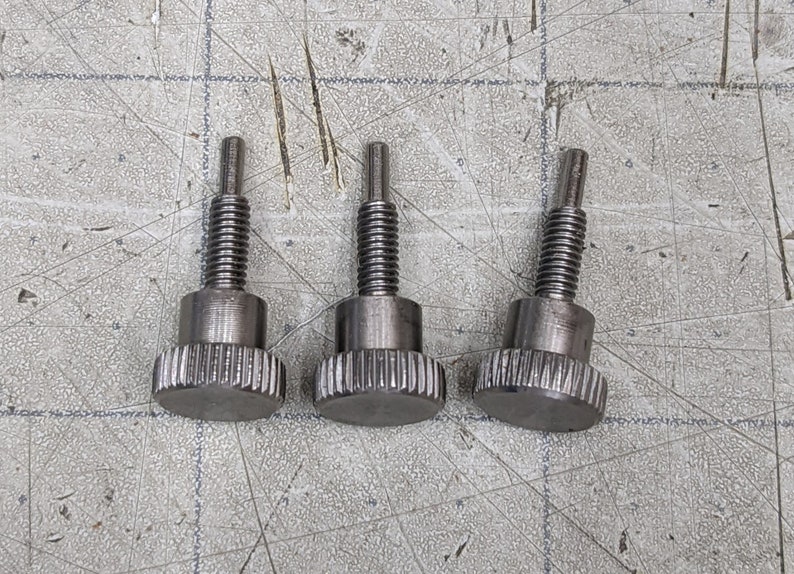 May include: Three silver thumbscrews with a knurled head and a threaded shaft.