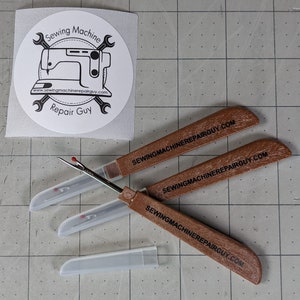 May include: Three brown wooden thread cutters with a clear plastic case. Each cutter has the text "sewingmachinerepairguy.com" printed on the handle.