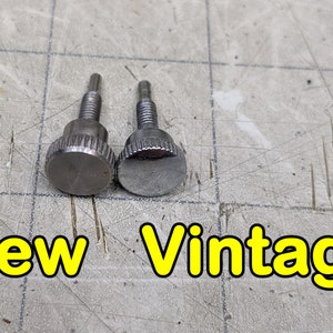 May include: Two silver metal screws with knurled heads. The screw on the left is labeled "New" and the screw on the right is labeled "Vintage".