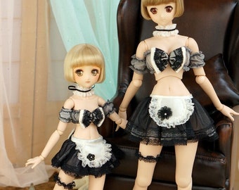 May include: Two dolls wearing black and white maid outfits. The dolls have blonde hair and are posed in a sitting and standing position. The doll in the standing position is sitting on a brown leather chair.