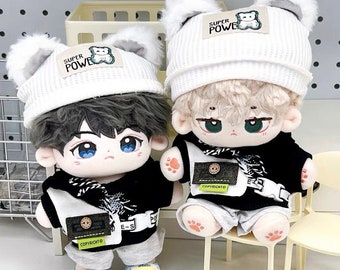 May include: Two plush toys wearing white beanies with bear ears and the text "Super Power" on the front. The toys are wearing black and white outfits with a graphic print and the text "Copyright" on the front. The toys are sitting on white chairs.