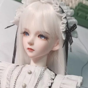 May include: A white doll with long, straight, white hair wearing a white dress with black trim and a white lace headband with a black bow.