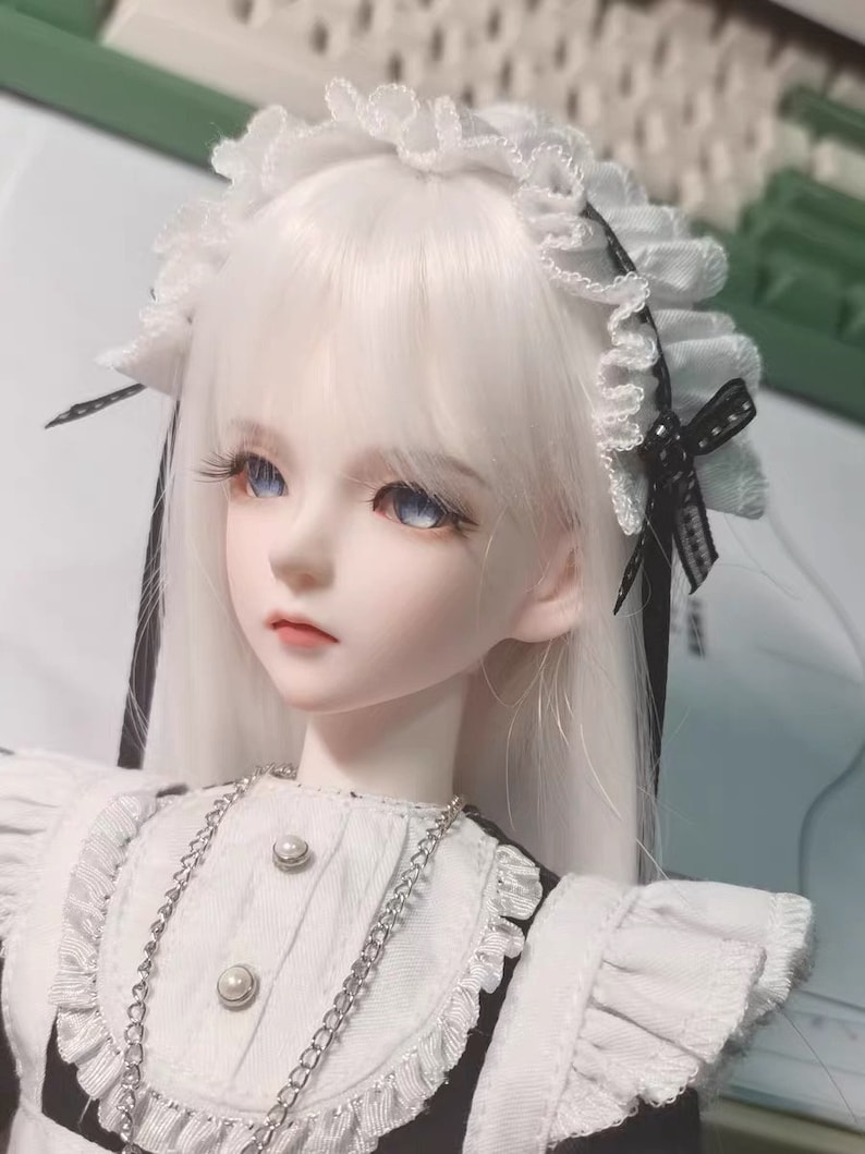 May include: A white doll with long, straight, white hair wearing a white dress with black trim and a white lace headband with a black bow.