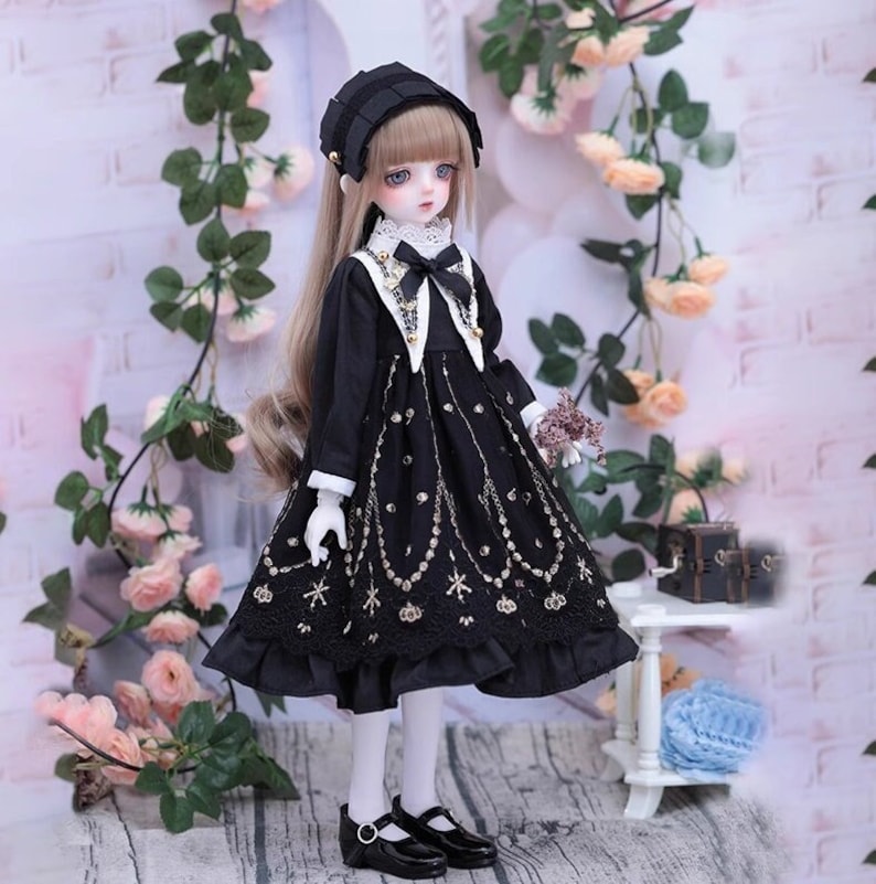 May include: A doll dressed in a black dress with gold accents, a matching hat, and black shoes. The dress features a detailed pattern and white cuffs. The doll has long blonde hair and is posed in front of a floral background.