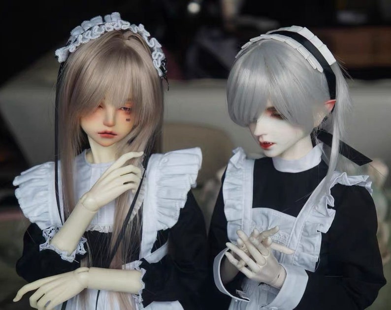 May include: Two dolls wearing black and white maid outfits. One doll has long, light brown hair with a white lace headband and black ribbons. The other doll has short, silver hair with a white lace headband and black ribbon.