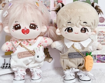 May include: Two plush dolls wearing different outfits. The doll on the left is wearing a pink and white dress with a white overall and a bunny charm. The doll on the right is wearing a white shirt with a brown overall and a carrot charm. Both dolls have white sneakers.