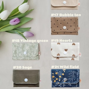 May include: A selection of small fabric wallets in various colours and patterns. The wallets include options in nude, bubble tea, vintage green, hearts, sage, and wild field designs. Each wallet has a snap closure and a small tag.