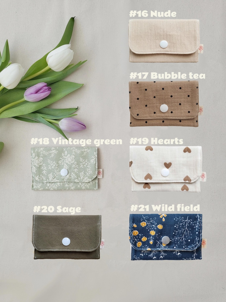 May include: A selection of small fabric wallets in various colours and patterns. The wallets include options in nude, bubble tea, vintage green, hearts, sage, and wild field designs. Each wallet has a snap closure and a small tag.