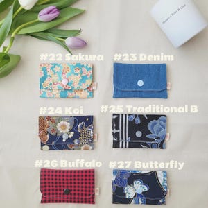 May include: A selection of small fabric wallets with diverse patterns and colours. Designs feature floral, denim, koi fish, buffalo plaid, and butterfly patterns. Each wallet has a button closure. The text "#22 Sakura", "#23 Denim", "#24 Koi", "#25 Traditional B", "#26 Buffalo", and "#27 Butterfly" is visible.