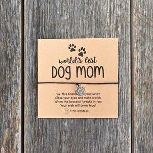 May include: A brown card with the text "world's best Dog mom" and a paw print charm attached to a black string bracelet. The card also includes instructions for making a wish when the bracelet breaks.