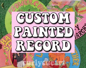 May include: A collection of custom-painted vinyl records. Each record features unique, colorful artwork with themes like flowers, dragons, and strawberries. The records are displayed on a green surface, with the text "CUSTOM PAINTED RECORD" in the center.