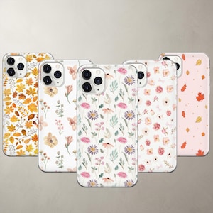 May include: Five smartphone cases featuring distinct patterns: one with yellow and orange autumn leaves, one with delicate peach flowers, one with purple and pink wildflowers, one with soft pink roses, and one with small orange and yellow leaves.
