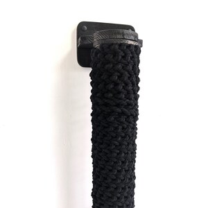 May include: Black rope door handle with a wooden base and a black metal mounting plate. The handle is mounted on a white wall.