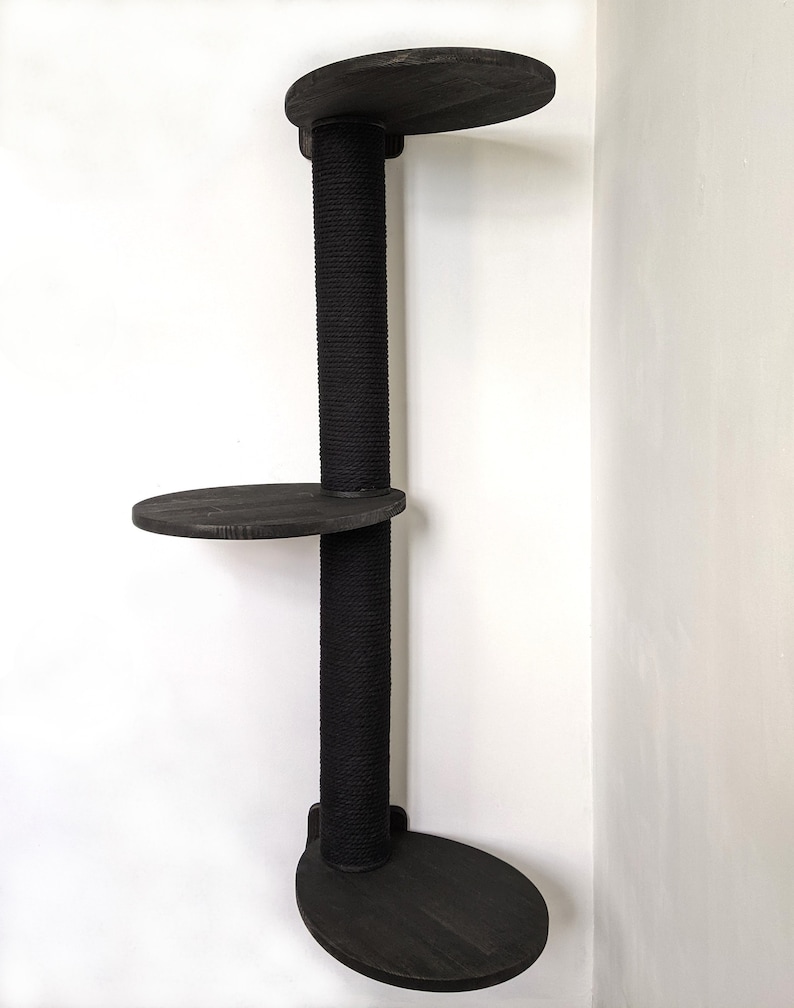May include: A black cat tree with three platforms and a sisal-covered scratching post. The platforms are round and made of wood. The cat tree is mounted on a wall.