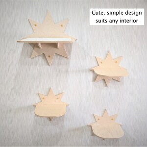 Op de afbeelding: Vier houten planken in de vorm van sterren, gemonteerd aan een witte muur. De planken zijn gemaakt van licht hout en hebben een eenvoudig ontwerp. De tekst "Cute, simple design suits any interior" staat op de muur boven de planken.