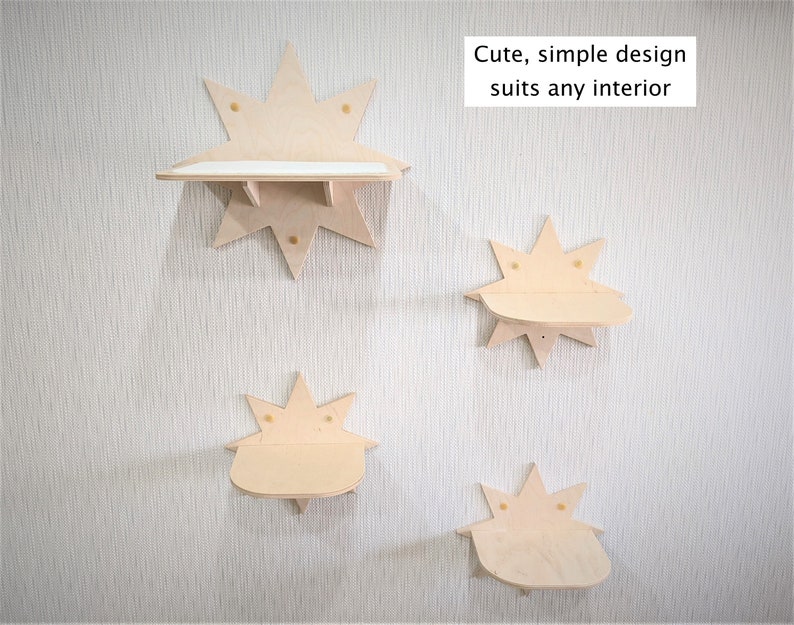 Op de afbeelding: Vier houten planken in de vorm van sterren, gemonteerd aan een witte muur. De planken zijn gemaakt van licht hout en hebben een eenvoudig ontwerp. De tekst "Cute, simple design suits any interior" staat op de muur boven de planken.