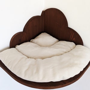 May include: A wooden cat bed shaped like a cloud, with a white cushion inside. The bed is mounted on a wall corner.