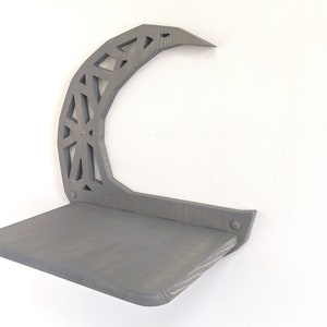 Pode incluir: Uma prateleira de madeira cinza com um design de lua crescente. A prateleira &eacute; fixada na parede e tem uma superf&iacute;cie plana para exibir itens.