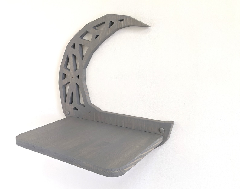 Pode incluir: Uma prateleira de madeira cinza com um design de lua crescente. A prateleira &eacute; fixada na parede e tem uma superf&iacute;cie plana para exibir itens.