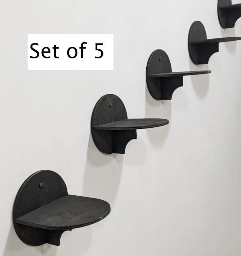 May include: Set of five black wooden wall shelves in a staggered formation. The shelves are rounded and have a slight lip on the front edge.  "Set of 5" is written in white text on a white background.