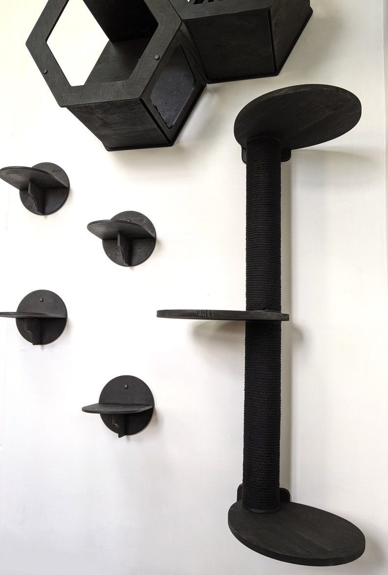 May include: Black cat tree with multiple platforms and a scratching post. The platforms are round and attached to a wall. The scratching post is covered in rope.