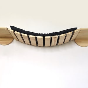 May include: A wooden cat bridge with a black cushion. The bridge is curved and has a slatted design. The bridge is mounted to a wall.