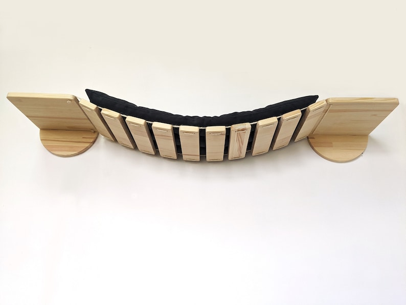 May include: A wooden cat bridge with a black cushion. The bridge is curved and has a slatted design. The bridge is mounted to a wall.