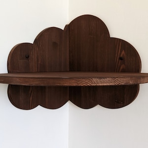 May include: A dark brown wooden corner shelf shaped like a cloud. The shelf has a scalloped edge and is mounted on a white wall.