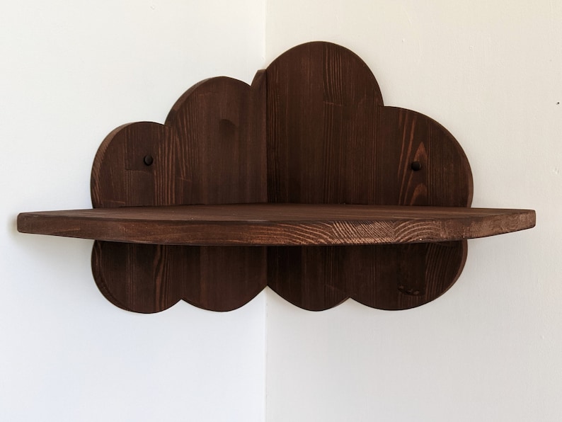 May include: A dark brown wooden corner shelf shaped like a cloud. The shelf has a scalloped edge and is mounted on a white wall.