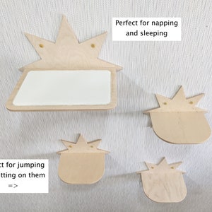 Op de afbeelding: Vier houten kattenplanken in de vorm van een ster. De planken zijn gemonteerd aan een witte muur. De bovenste plank is groter en heeft een vlak oppervlak. De andere drie planken zijn kleiner en hebben een gebogen oppervlak. De tekst "Perfect om te dutten en te slapen" staat op een wit rechthoek boven de bovenste plank. De tekst "Perfect om op te springen en te zitten =>" staat op een wit rechthoek onder de onderste plank.