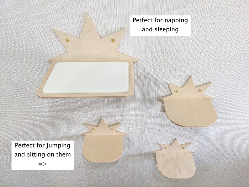 Op de afbeelding: Vier houten kattenplanken in de vorm van een ster. De planken zijn gemonteerd aan een witte muur. De bovenste plank is groter en heeft een vlak oppervlak. De andere drie planken zijn kleiner en hebben een gebogen oppervlak. De tekst "Perfect om te dutten en te slapen" staat op een wit rechthoek boven de bovenste plank. De tekst "Perfect om op te springen en te zitten =>" staat op een wit rechthoek onder de onderste plank.