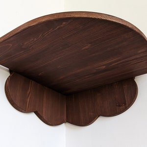 May include: A dark brown wooden corner shelf with a curved top and scalloped edges. The shelf is made of solid wood and has a rustic finish.