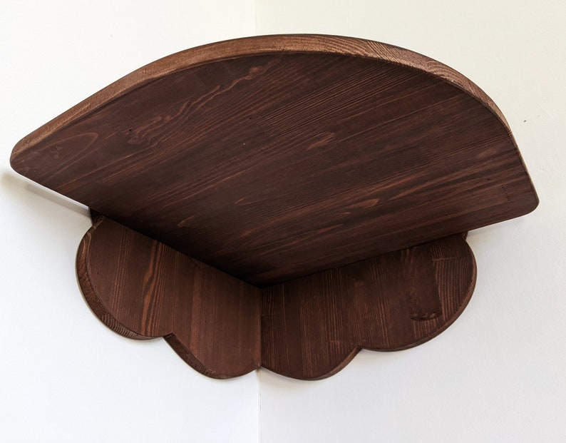 May include: A dark brown wooden corner shelf with a curved top and scalloped edges. The shelf is made of solid wood and has a rustic finish.