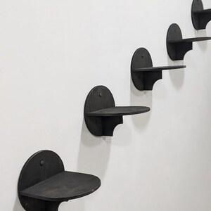 May include: Five black wooden wall shelves in a staggered formation. Each shelf is a semi-circle with a flat surface and a curved edge.