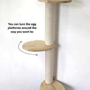 Pu&ograve; includere: Un albero per gatti da parete con finitura in legno naturale e un palo per grattare rivestito in sisal. Le piattaforme hanno la forma di un uovo e possono essere ruotate in diverse posizioni. Il testo "You can turn the egg platforms around the way you want to:" &egrave; visibile nell'immagine.
