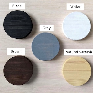 May include: Five wooden circles painted in different colors: black, white, gray, brown, and natural varnish. The circles are arranged in a semi-circle on a light wood surface.