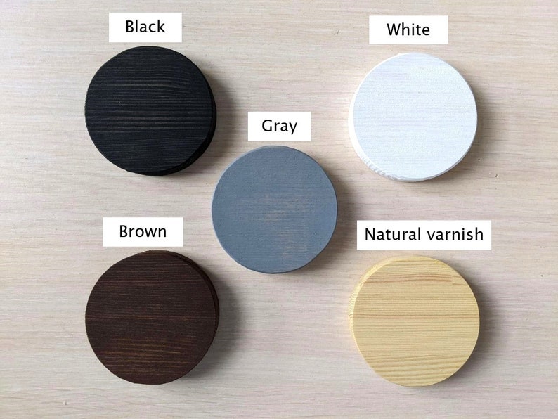 May include: Five wooden circles painted in different colors: black, white, gray, brown, and natural varnish. The circles are arranged in a semi-circle on a light wood surface.