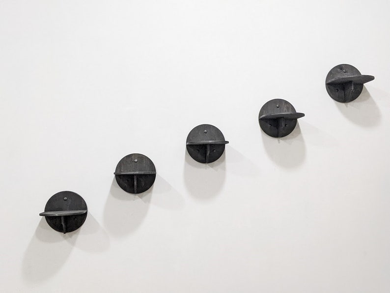 May include: Five black wooden wall shelves in a staggered pattern. Each shelf is a circle with a small shelf extending out from the side.