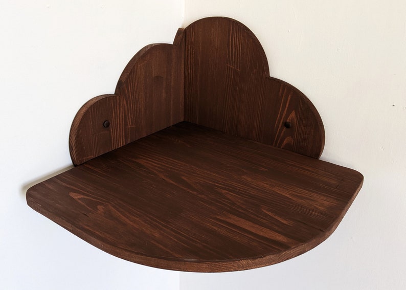 May include: A dark brown wooden corner shelf shaped like a cloud. The shelf has a rounded edge and is mounted on a white wall.