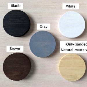 Op de afbeelding: Vijf houten cirkels in verschillende kleuren: zwart, wit, grijs, bruin en naturel hout. De tekst "Only sanded or Natural matte waxed" staat onder de cirkels.