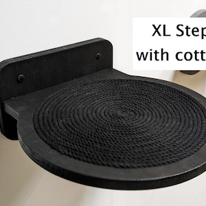 May include: Black wooden cat step with a round, black rope-covered surface. The step is mounted to a wall and labeled "XL Step with cotton".